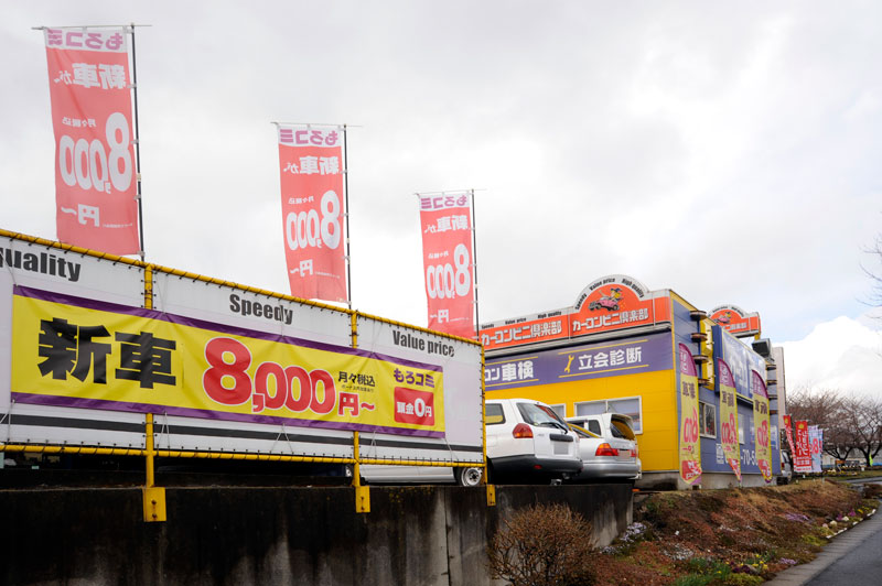 道路側面に大きくもろコミを宣伝!店舗の青い外壁にはカーコン車検も対応していること大きく掲げています!